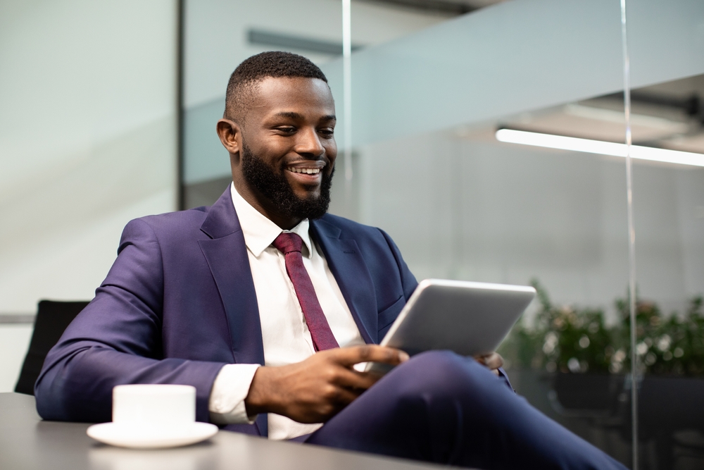 Cheerful,Bearded,Black,Businessman,Sitting,At,Workdesk,,Drinking,Coffee,And